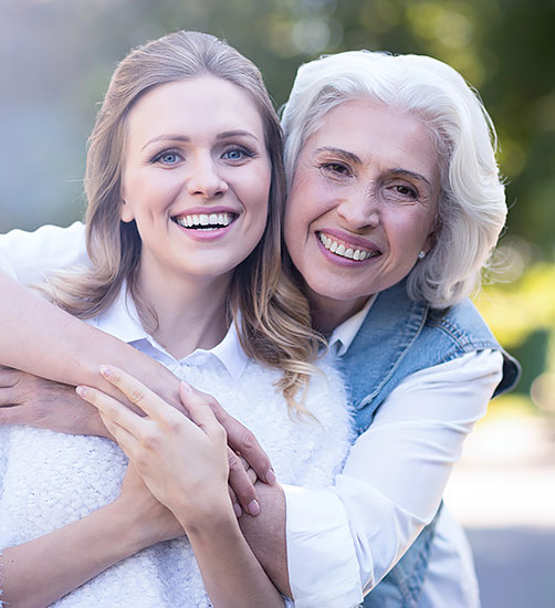 Happy mother and daughter smiling confidently after receiving dental bridges and crowns.